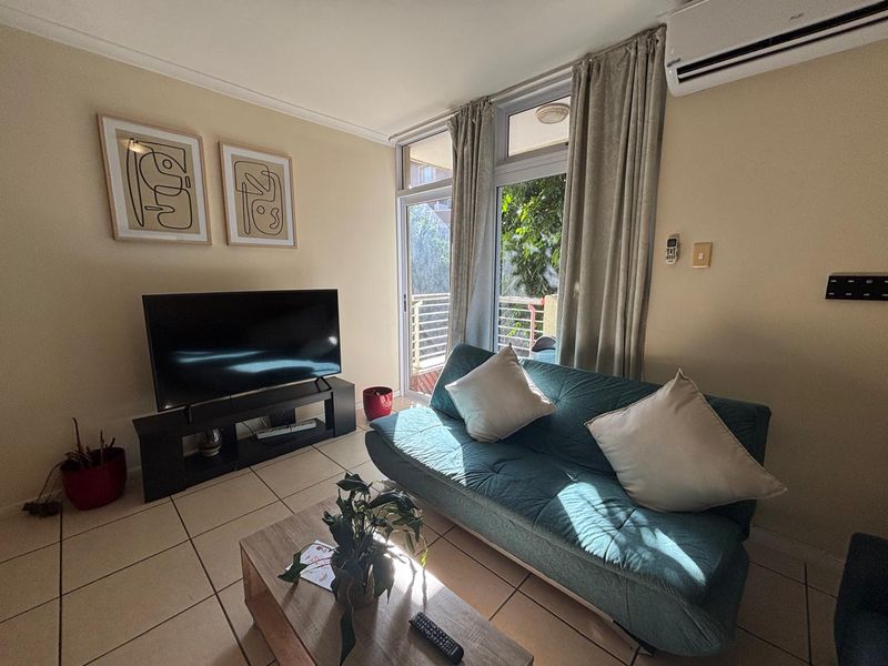 A compact living room featuring tiled flooring, a wall-mounted air conditioning unit, and a sliding glass door providing access to an outdoor area.