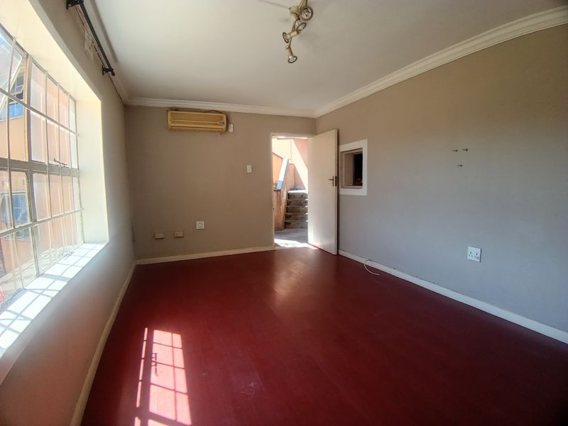A vacant living room featuring red-toned flooring, a wall-mounted air conditioning unit, and natural light from a large side window.