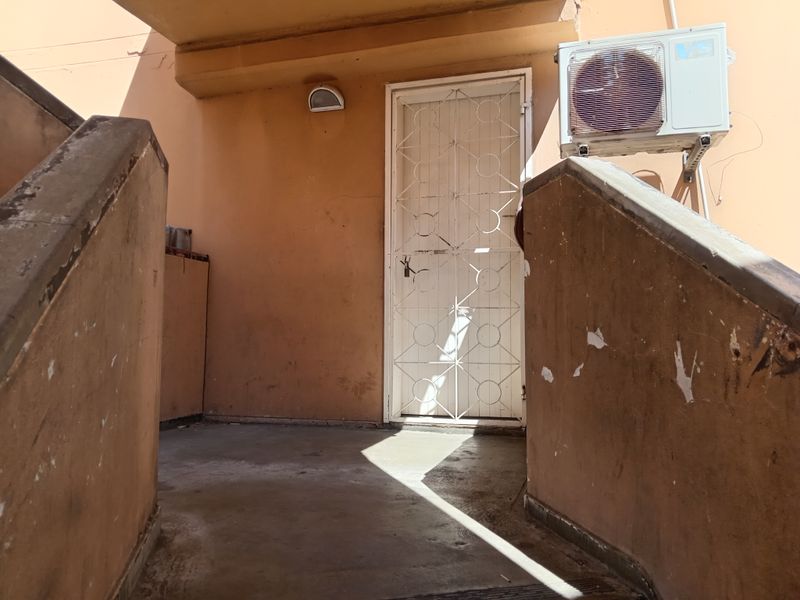 Exterior entrance area featuring a security gate, concrete staircase, and wall-mounted air conditioning unit.