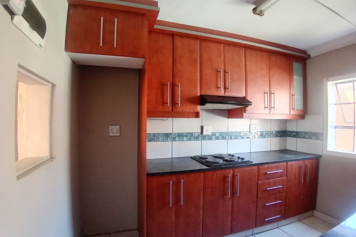 A functional kitchen featuring warm-toned wooden cabinetry, dark granite countertops, a built-in electric hob, and a tiled backsplash.
