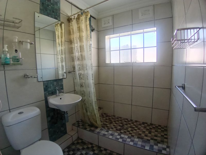 A functional bathroom featuring a raised shower cubicle with mosaic tiling, a wall-mounted basin, and a standard toilet.