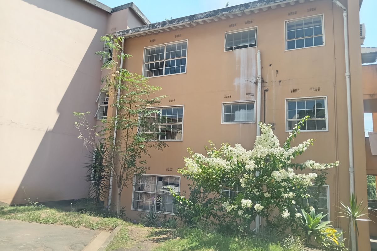 Exterior view of the apartment building facade showing multi-level windows and established garden landscaping.