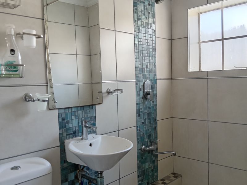 A functional bathroom featuring a wall-mounted basin, a raised shower enclosure with mosaic tile accents, and a standard toilet.