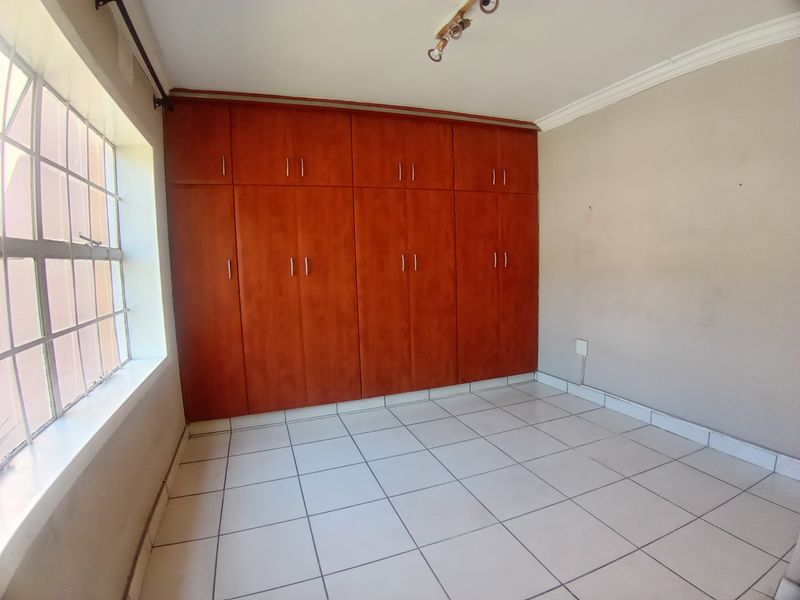 A bedroom featuring built-in wooden cupboards, tiled flooring, and a large window providing natural light.