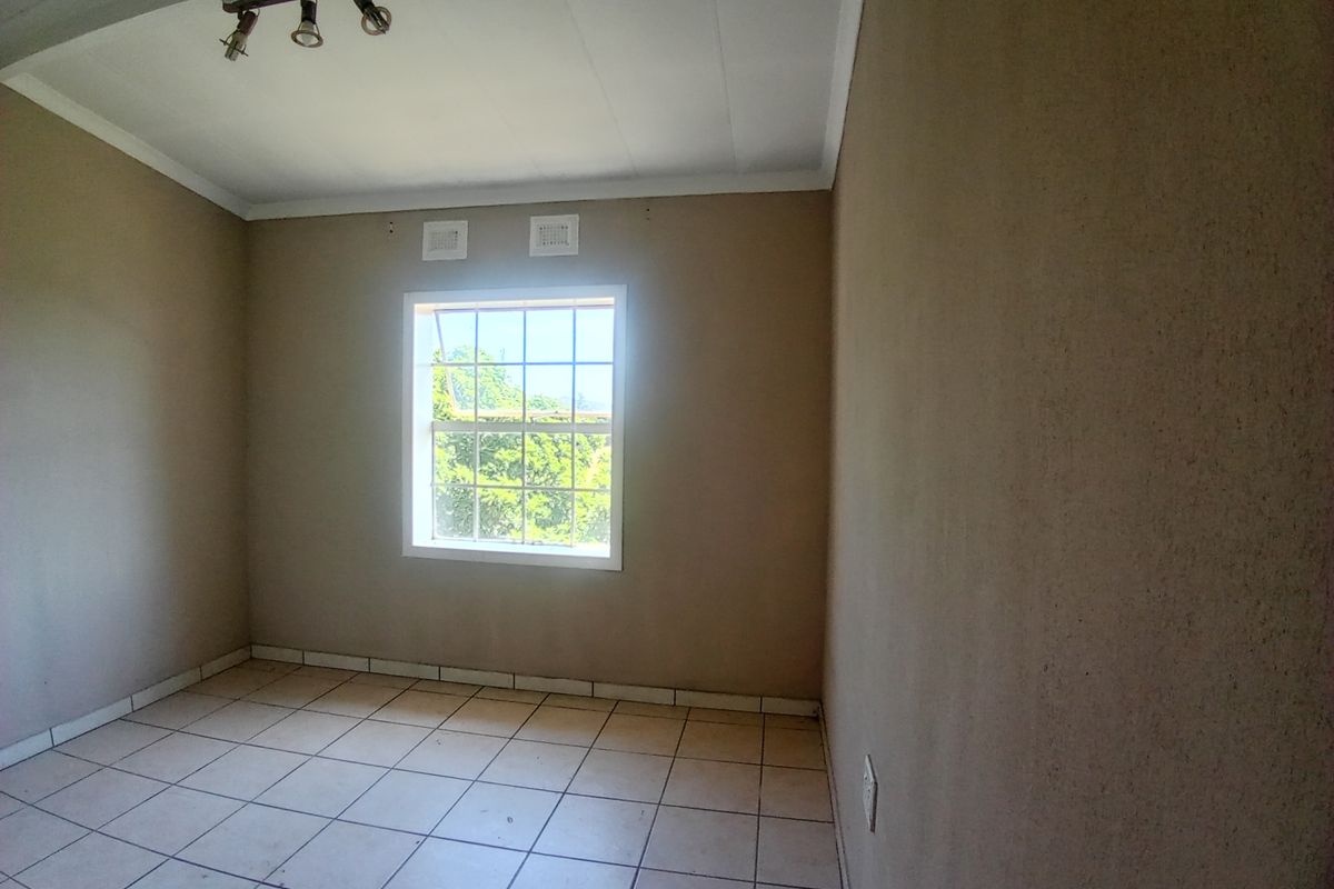 An empty bedroom featuring neutral wall tones, tiled flooring, and a window providing natural light.