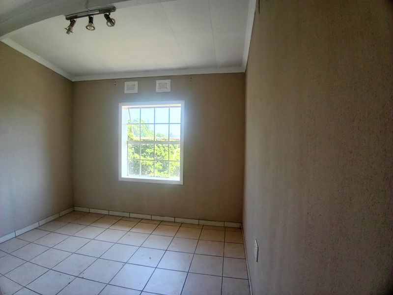 An empty bedroom featuring neutral wall tones, tiled flooring, and a window providing natural light.