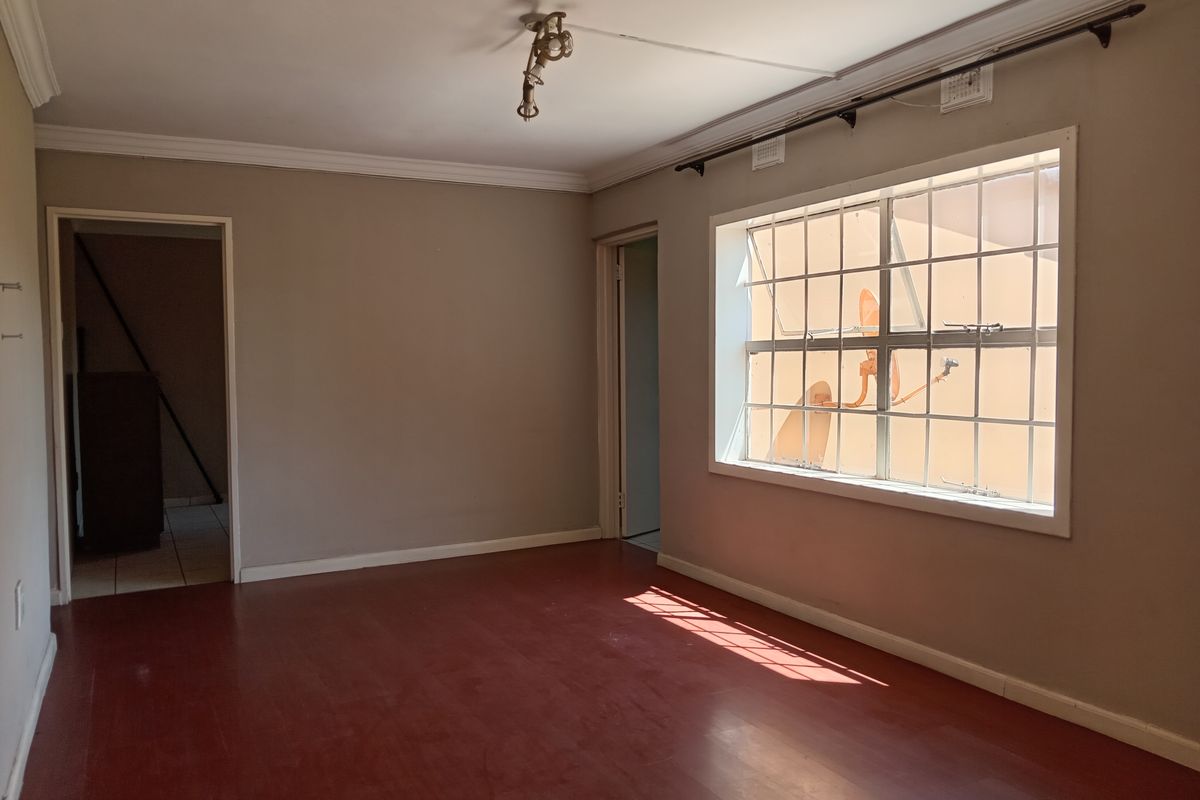 An empty living room featuring painted flooring, crown molding, and a large window with security bars, offering a blank canvas for renovation.