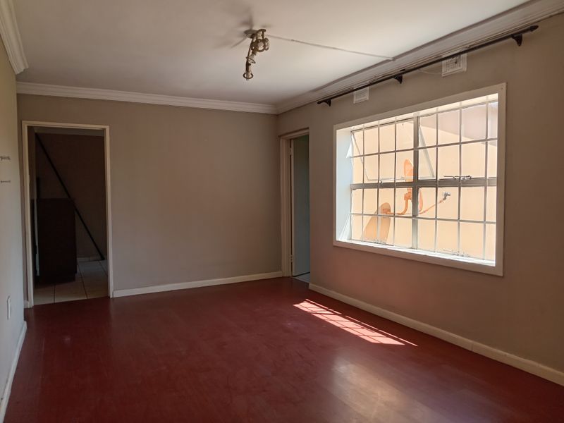 An empty living room featuring painted flooring, crown molding, and a large window with security bars, offering a blank canvas for renovation.
