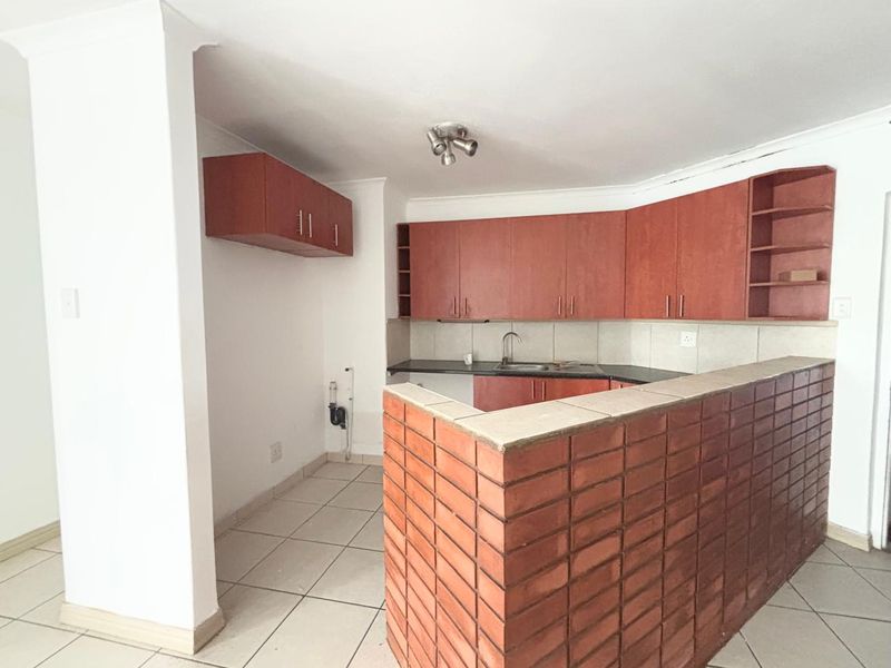 A functional kitchen featuring built-in wooden cabinetry, a brick breakfast bar, and tiled flooring, offering a blank canvas for potential modern updates.