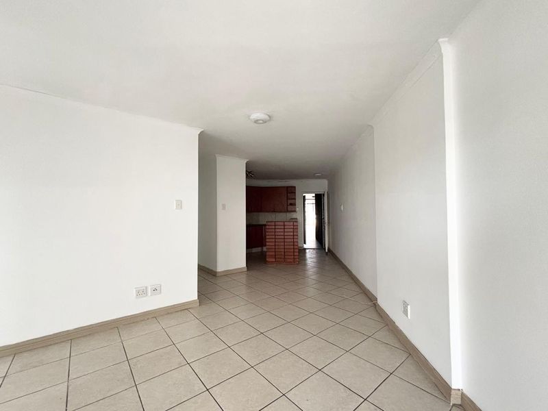 An empty open-plan living and kitchen area featuring neutral ceramic floor tiles and basic kitchen cabinetry.