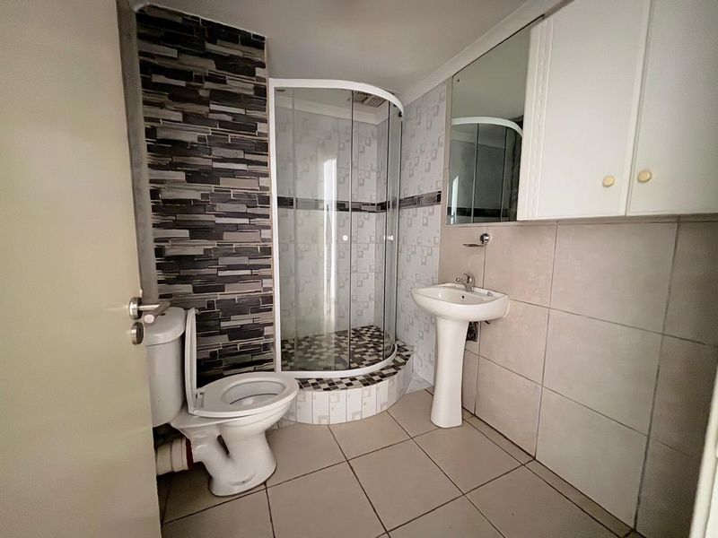 A functional bathroom featuring a corner shower enclosure, pedestal basin, toilet, and wall-mounted storage cabinet with tiled finishes throughout.