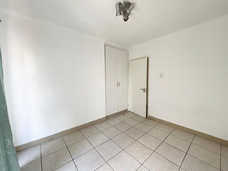 A vacant bedroom featuring neutral white walls, tiled flooring, and a built-in wardrobe, offering a clean canvas for personalization.