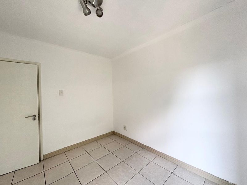 A clean, empty bedroom featuring neutral tiled flooring, white walls, and a modern ceiling-mounted spotlight fixture.