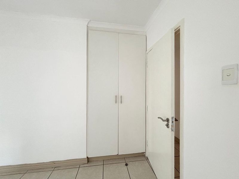A clean, empty bedroom featuring neutral tiled flooring, built-in cupboards, and white walls, providing a blank canvas for personalization.