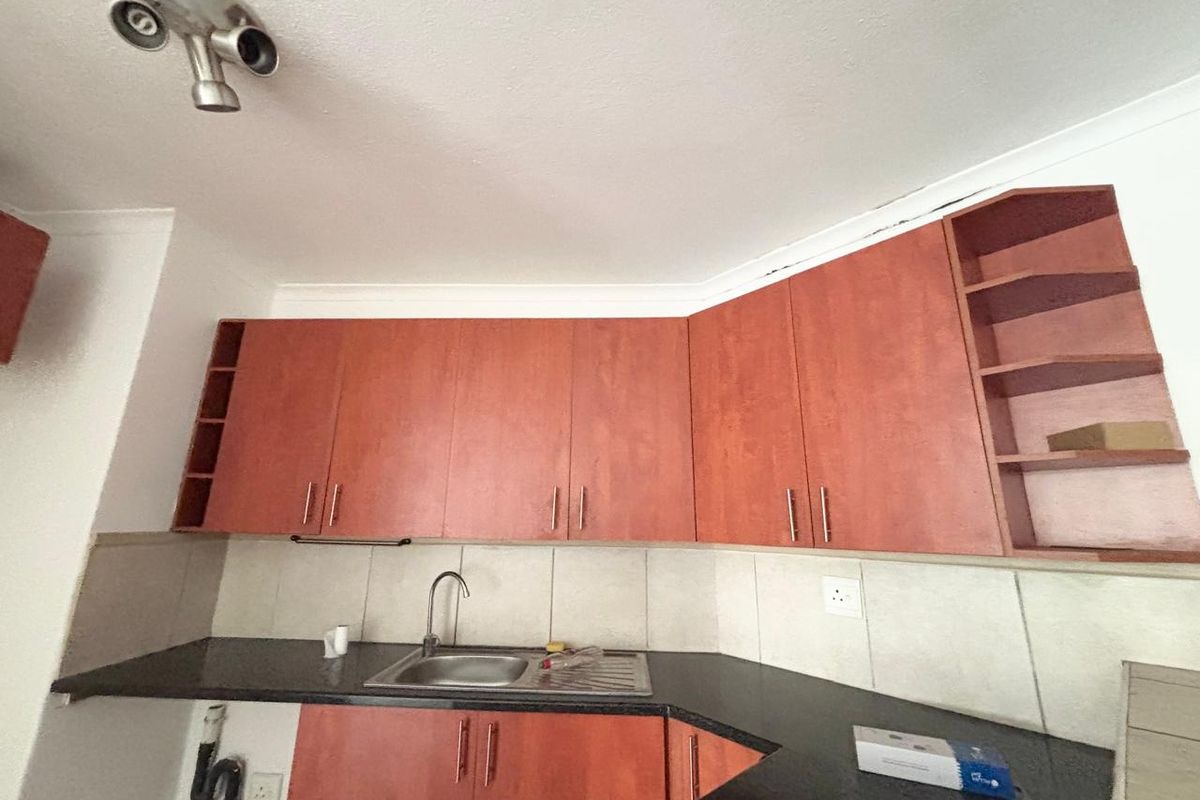 A functional kitchen featuring wood-look cabinetry, dark granite countertops, a stainless steel sink, and tiled backsplash, offering a practical layout for culinary tasks.