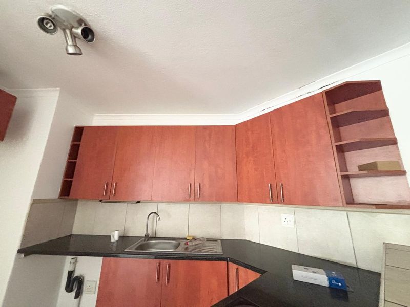 A functional kitchen featuring wood-look cabinetry, dark granite countertops, a stainless steel sink, and tiled backsplash, offering a practical layout for culinary tasks.