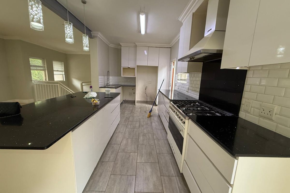 Modern kitchen featuring a large central island with black stone countertops, white cabinetry, subway tile backsplash, and a built-in gas stove with extractor fan.
