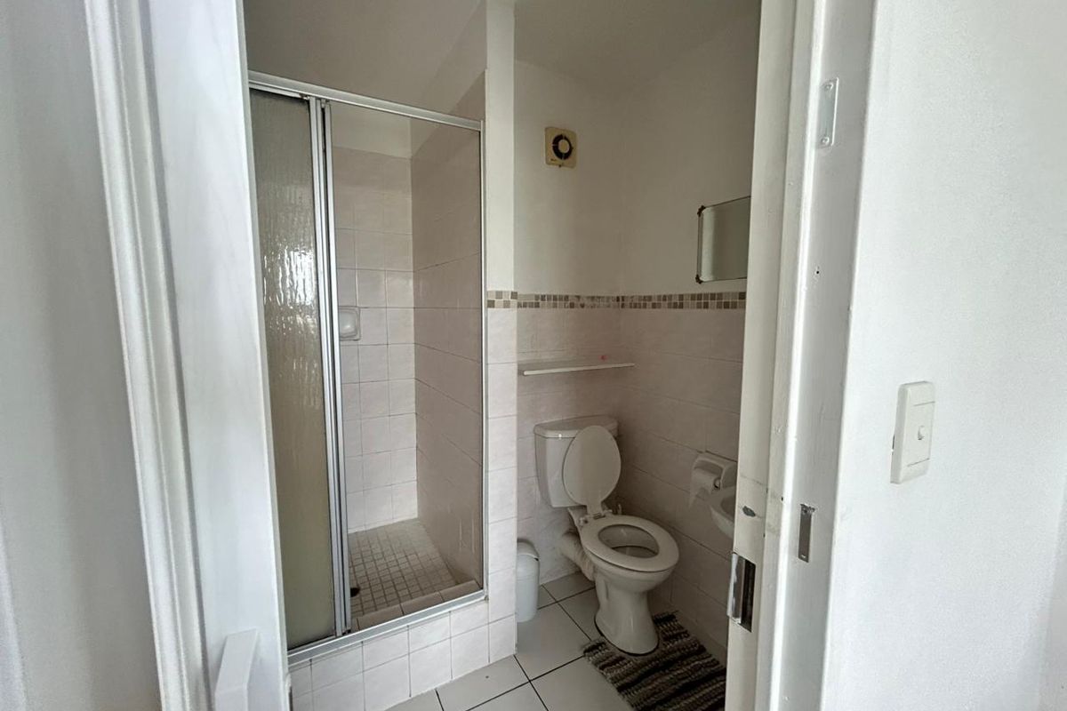 A functional bathroom featuring a glass-enclosed shower, toilet, and wall-mounted basin with neutral tiling.