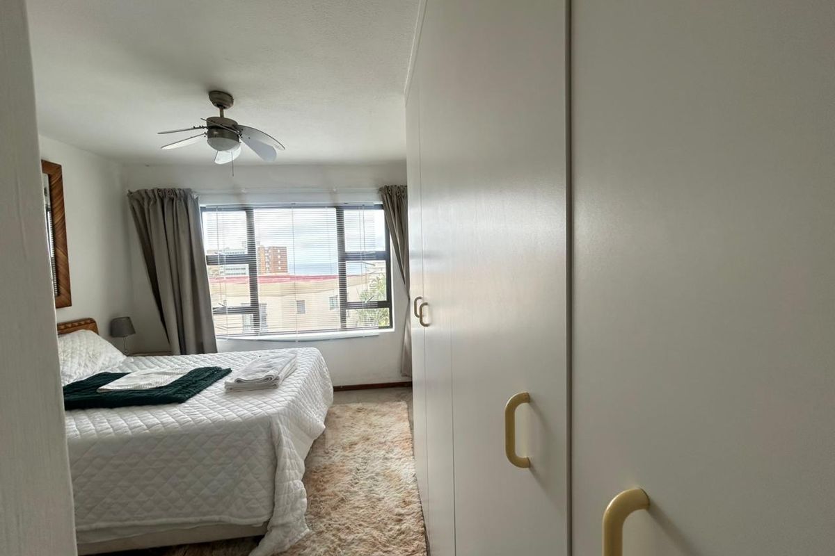A bedroom featuring built-in floor-to-ceiling wardrobes, a ceiling fan, and a window with natural light.