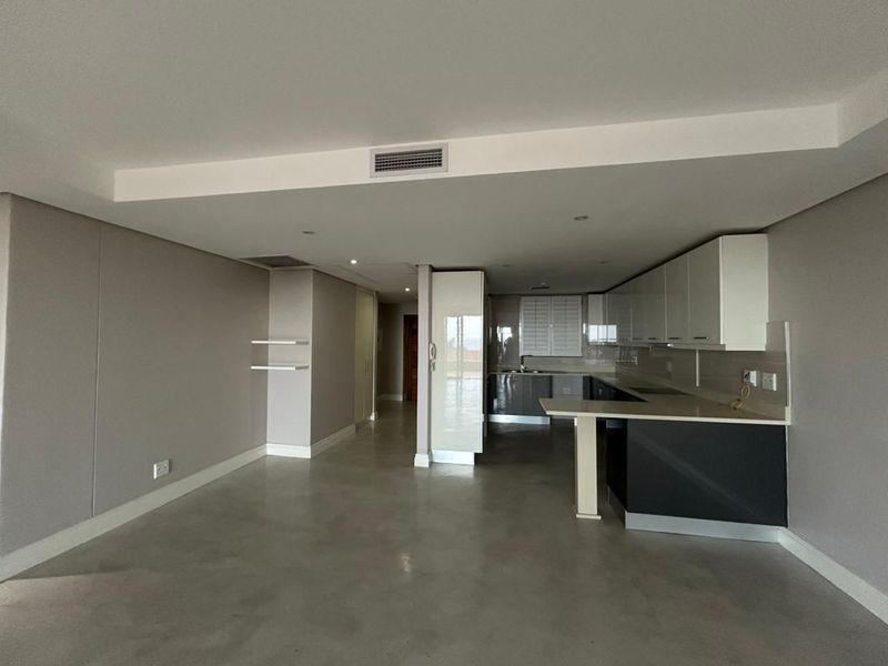 A spacious open-plan living and kitchen area featuring modern cabinetry, stone countertops, a breakfast bar, and polished concrete flooring throughout.
