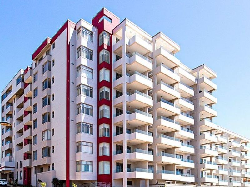 A modern multi-story apartment building featuring a prominent red accent facade and multiple private balconies with glass balustrades.