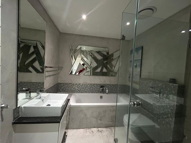 Modern bathroom featuring a built-in vanity with basin, a bathtub, and a separate glass-enclosed shower with contemporary mosaic tile accents.