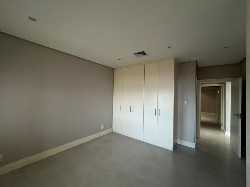 A clean, empty bedroom featuring neutral walls, polished concrete flooring, and ample built-in cupboard storage with recessed ceiling lighting.