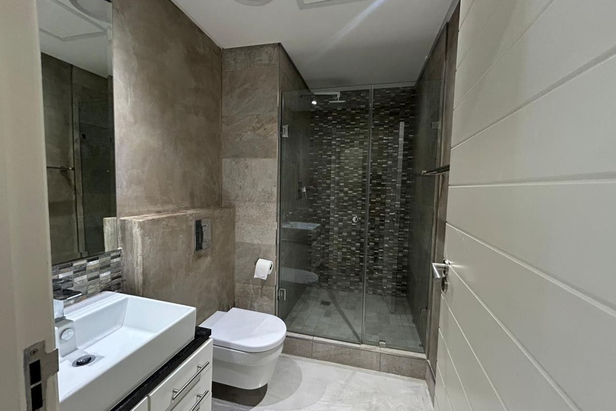Modern bathroom featuring a wall-mounted toilet, glass-enclosed shower with mosaic tile accents, and a sleek vanity with a vessel sink.
