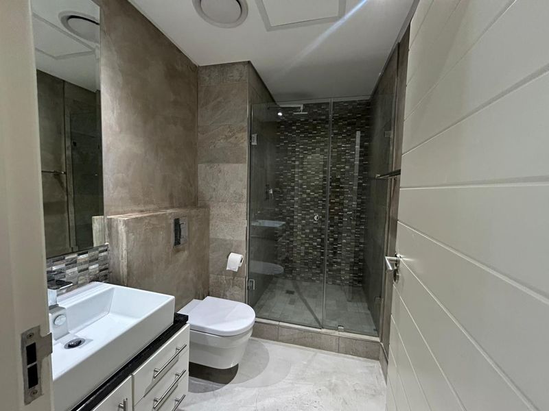 Modern bathroom featuring a wall-mounted toilet, glass-enclosed shower with mosaic tile accents, and a sleek vanity with a vessel sink.