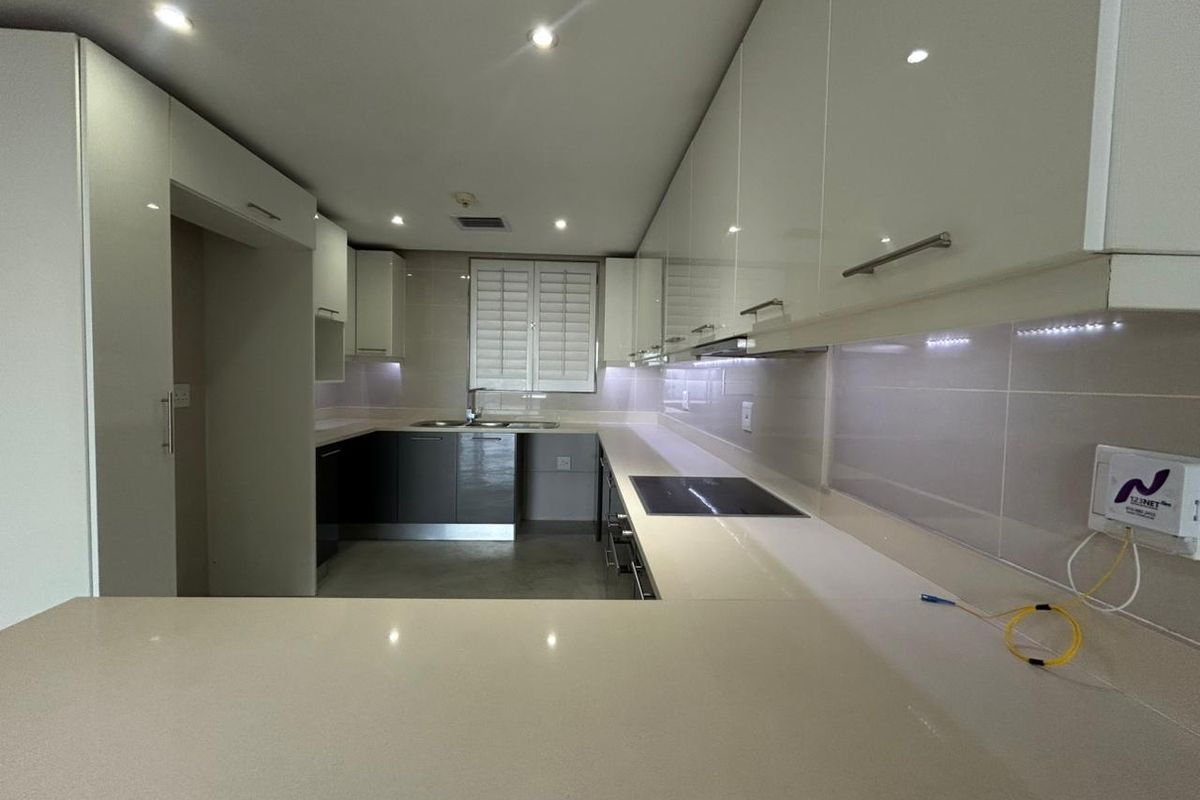 Modern kitchen featuring sleek high-gloss cabinetry, stone countertops, integrated electric hob, and recessed lighting in a clean, contemporary layout.