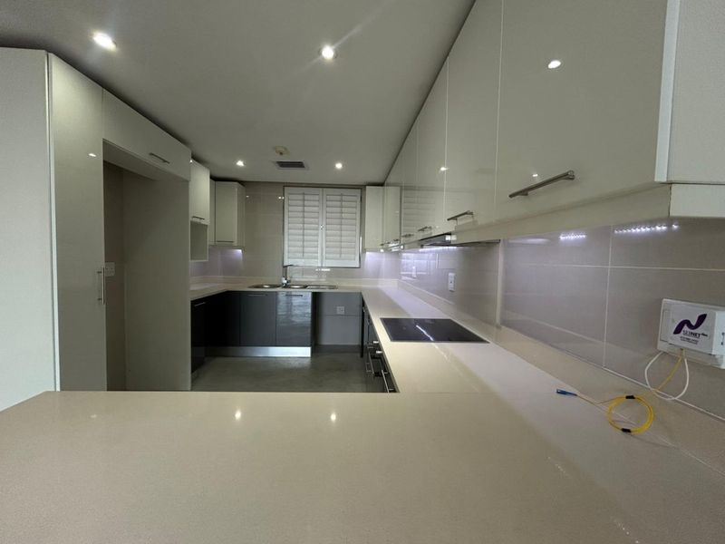 Modern kitchen featuring sleek high-gloss cabinetry, stone countertops, integrated electric hob, and recessed lighting in a clean, contemporary layout.