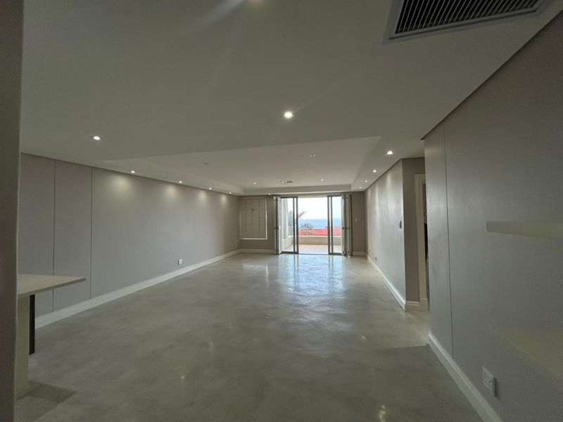 Spacious open-plan living area featuring polished concrete floors, recessed lighting, and bi-fold doors leading to an outdoor balcony with ocean views.