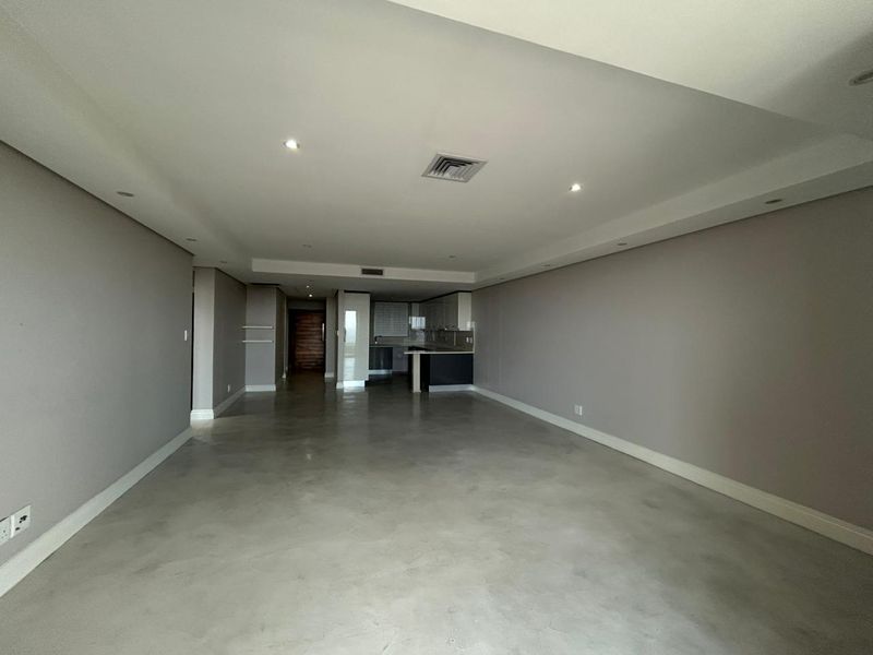 Spacious open-plan living area featuring polished concrete floors, recessed lighting, and a modern kitchen with built-in cabinetry.