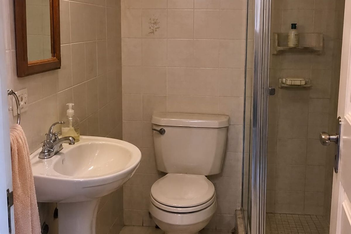 A functional bathroom featuring a pedestal sink, a standard toilet, and a glass-enclosed shower with tiled walls and flooring.