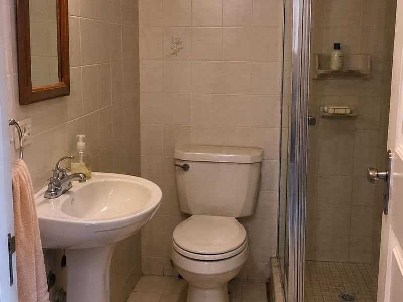 A functional bathroom featuring a pedestal sink, a standard toilet, and a glass-enclosed shower with tiled walls and flooring.