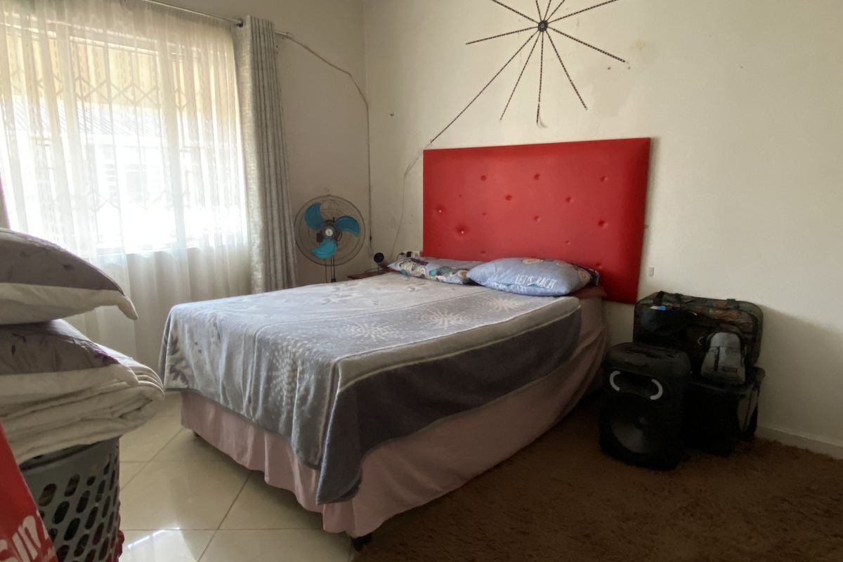 A bedroom featuring tiled flooring, a window with security bars, and neutral wall finishes.