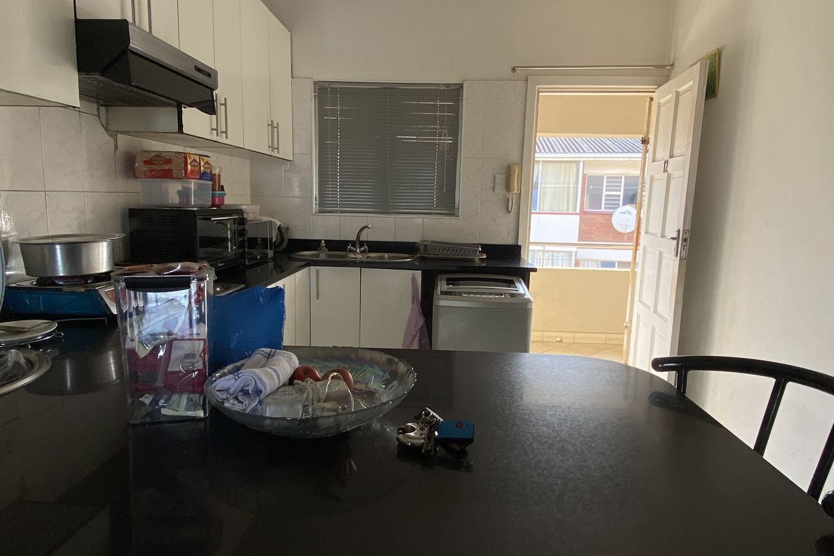 A functional kitchen featuring built-in cabinetry, dark countertops, a double sink, and an extractor fan, with direct access to an exterior balcony.