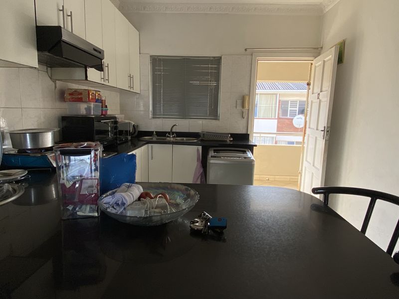 A functional kitchen featuring built-in cabinetry, dark countertops, a double sink, and an extractor fan, with direct access to an exterior balcony.