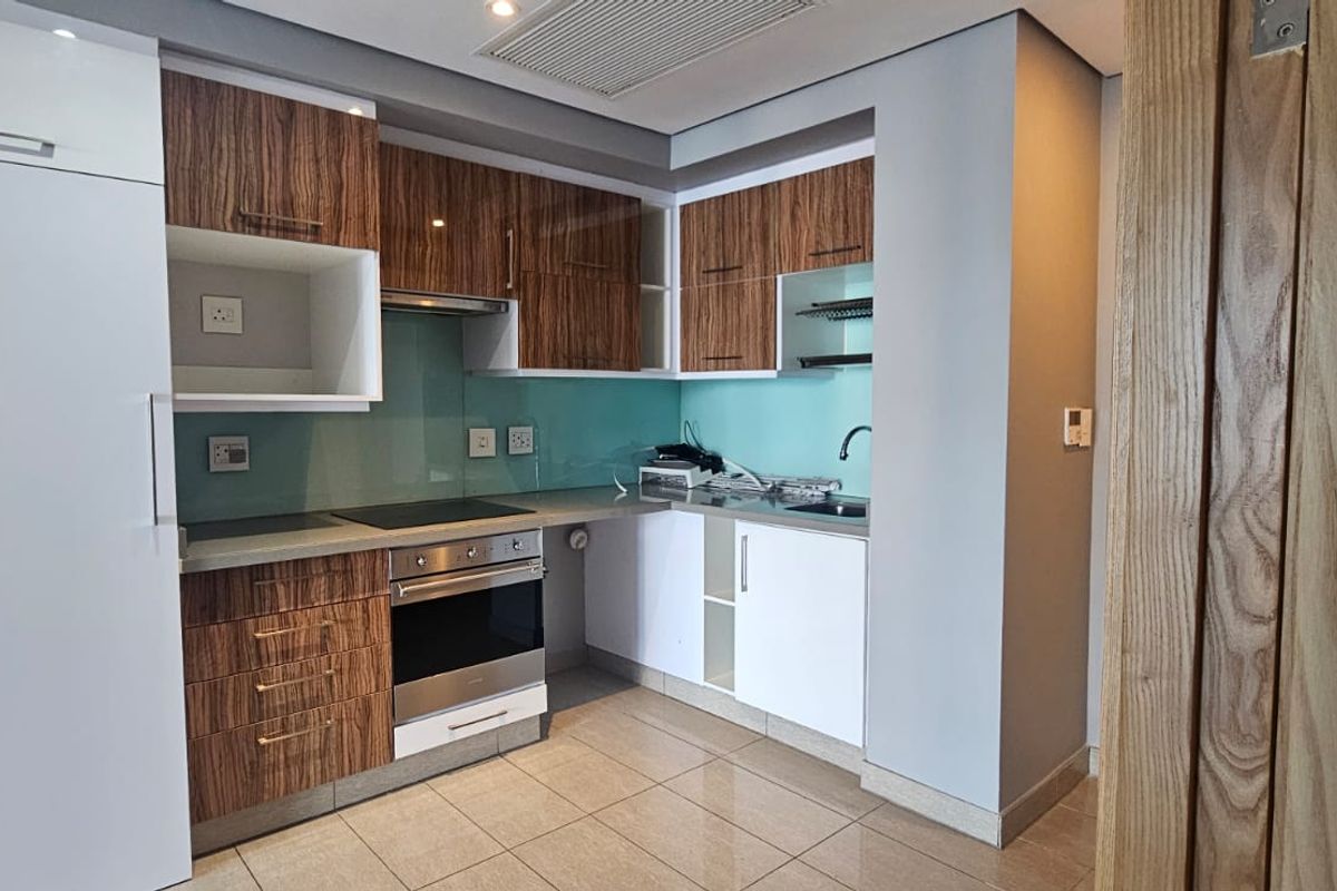 Modern kitchen featuring wood-grain and white cabinetry, glass splashback, integrated oven and hob, and tiled flooring in a clean, well-maintained space.