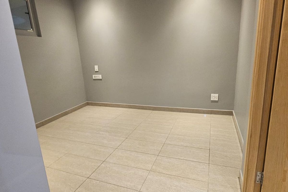 A clean, empty bedroom featuring neutral grey walls, tiled flooring, and recessed lighting, providing a versatile space ready for personalization.