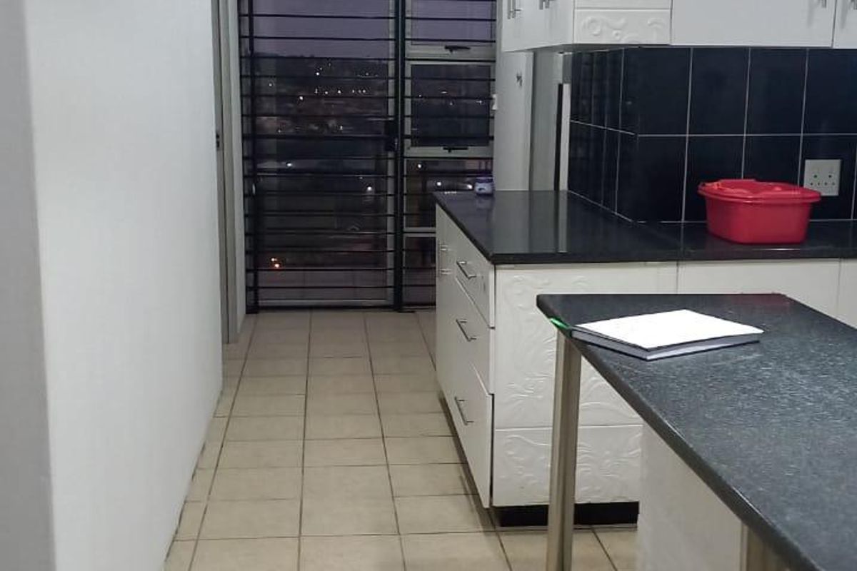 A functional kitchen featuring white cabinetry, dark granite countertops, tiled flooring, and a security gate leading to an outdoor area.