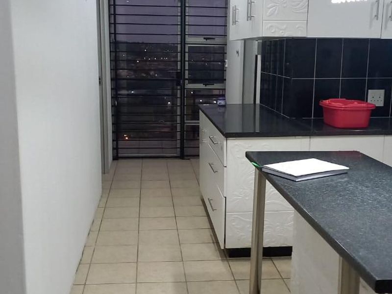 A functional kitchen featuring white cabinetry, dark granite countertops, tiled flooring, and a security gate leading to an outdoor area.