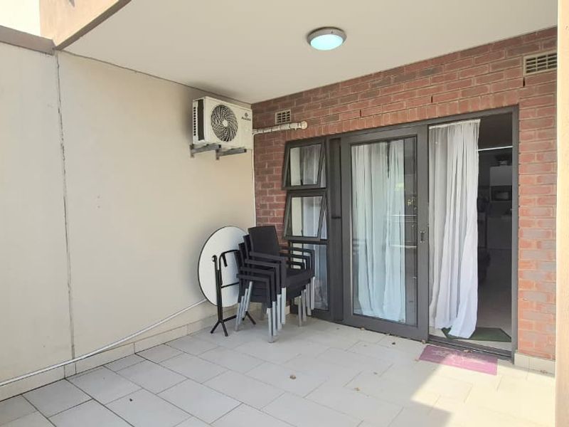 A covered balcony featuring tiled flooring, a brick accent wall, and a sliding glass door providing access to the interior living space.