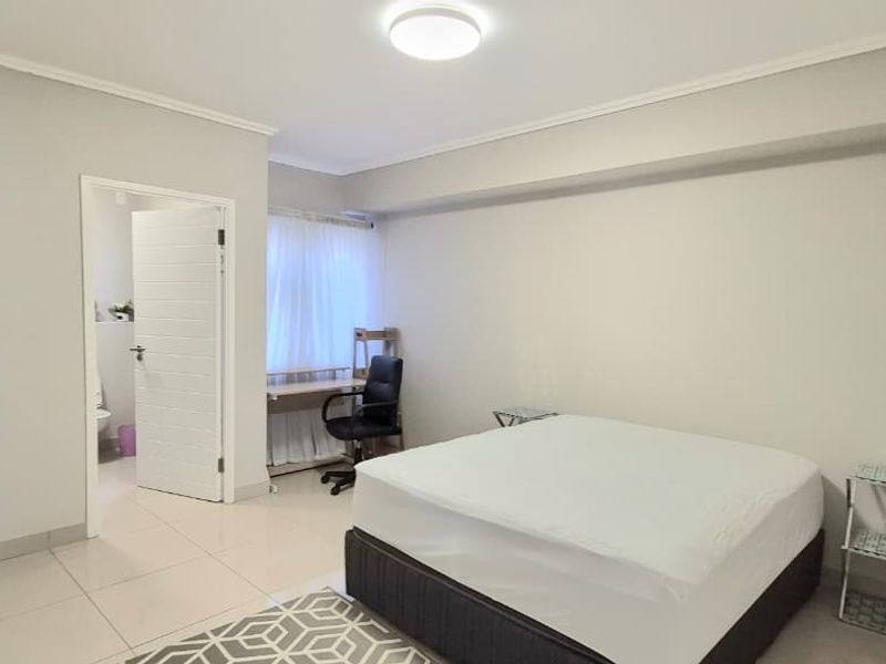 A clean and functional bedroom featuring tiled flooring, neutral walls, and an adjoining bathroom entrance.