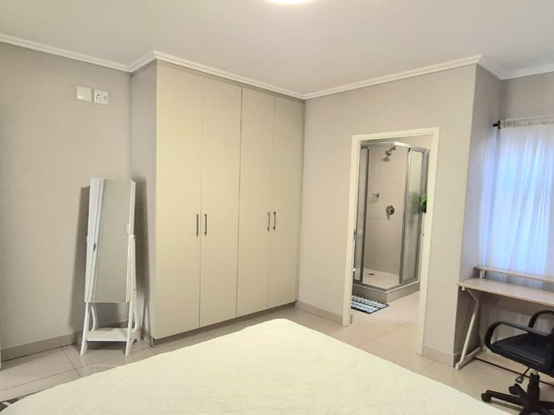 A well-maintained bedroom featuring built-in cupboards, tiled flooring, and an attached en-suite bathroom with a shower cubicle.