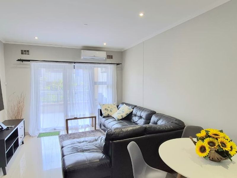 Open-plan living and dining area featuring tiled flooring, recessed downlighting, and a split-system air conditioner with direct access to a balcony.