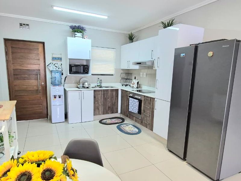 A functional kitchen featuring modern two-tone cabinetry, built-in oven and hob, extractor fan, and tiled flooring, providing a clean and practical cooking space.