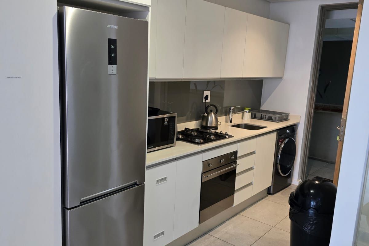 Modern galley-style kitchen featuring sleek white cabinetry, stainless steel appliances, gas hob, built-in oven, and tiled flooring.