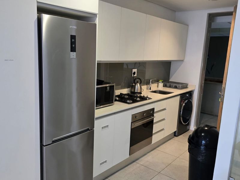Modern galley-style kitchen featuring sleek white cabinetry, stainless steel appliances, gas hob, built-in oven, and tiled flooring.