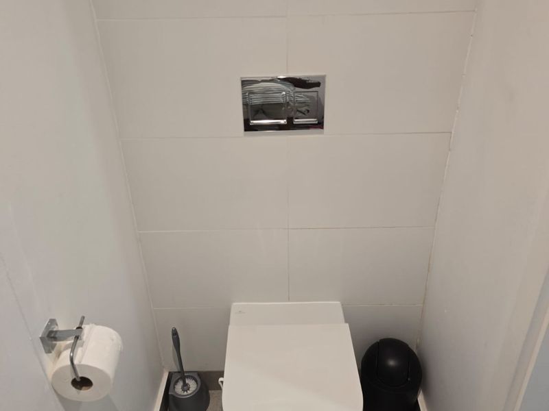 A clean and modern bathroom featuring a wall-mounted toilet with a concealed cistern and neutral tiled finishes.